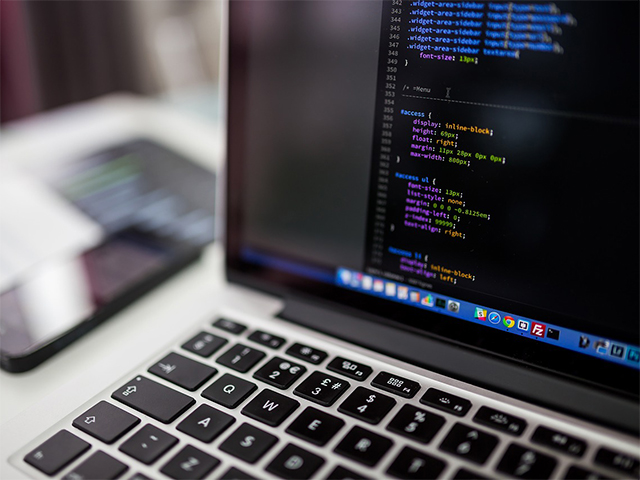 Macbook on desk, a persons hands are seen typing code.